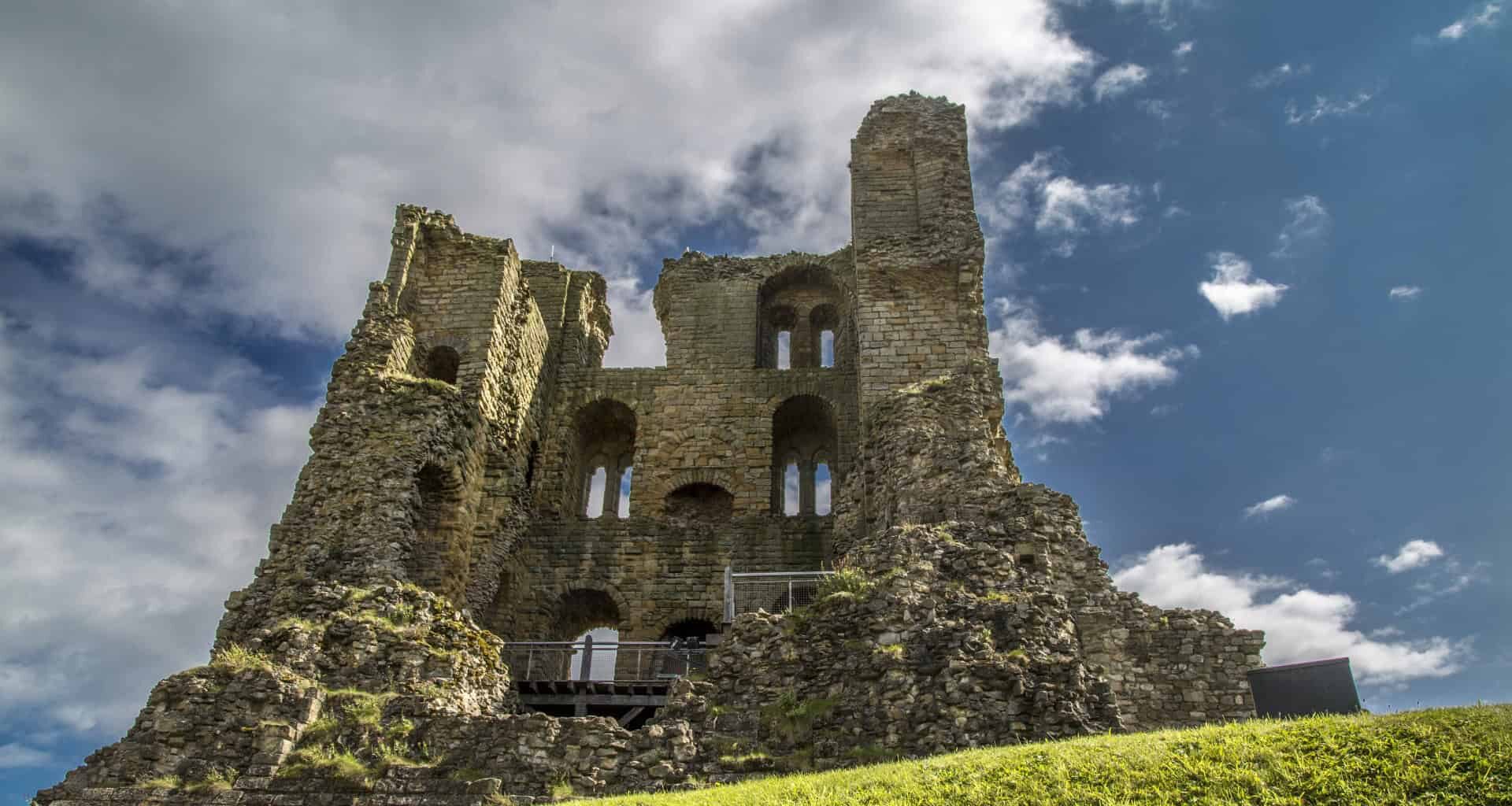 Ancient castle ruins with stone walls and arched windows under a cloudy sky.