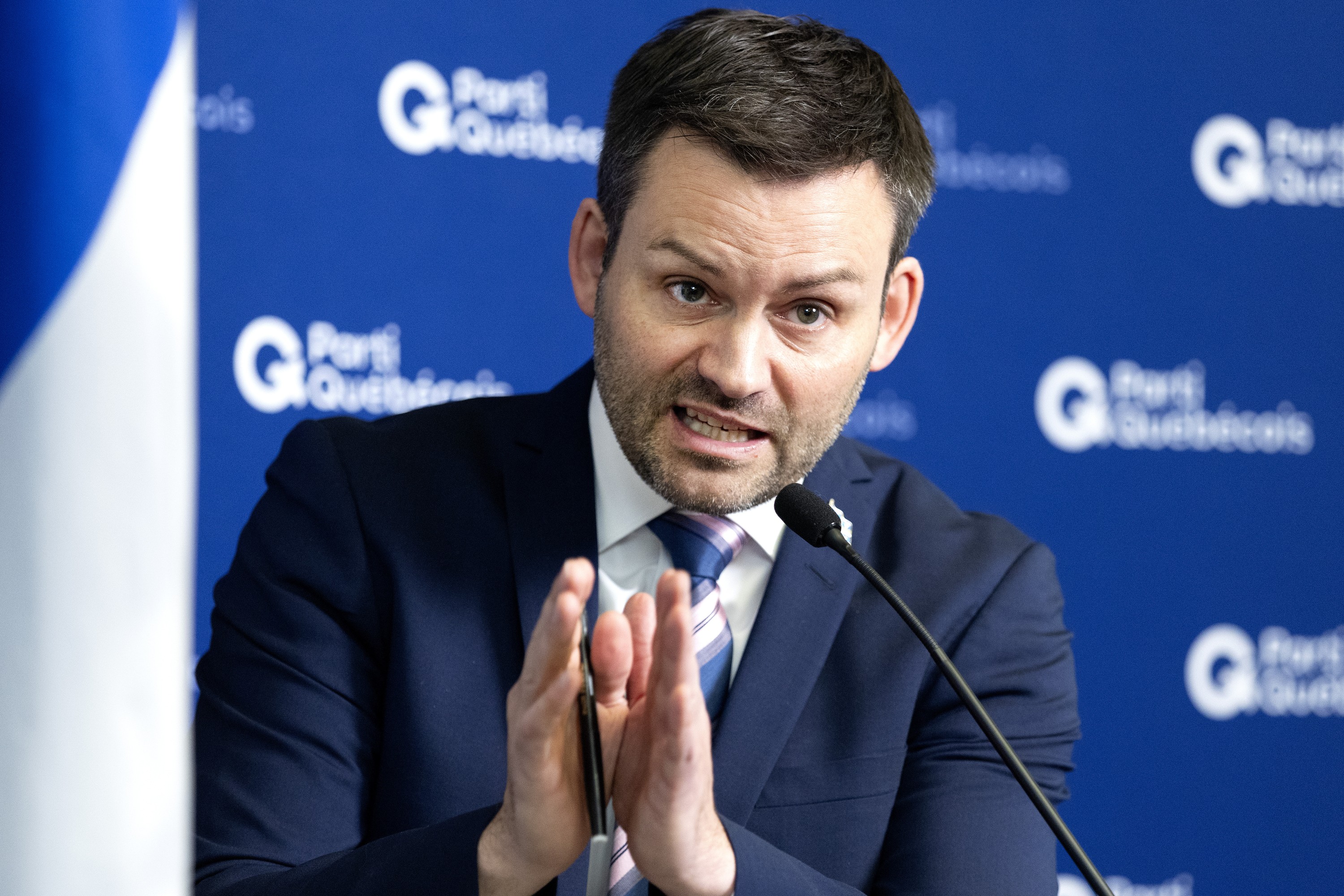 Parti Québécois Leader Paul St-Pierre Plamondon gestures as he speaks at a news conference, in front of a Parti Québécois backdrop.