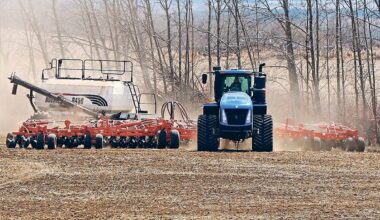 A large, blue, tracked tractor is pulling an air seeding rig toward the camera.
