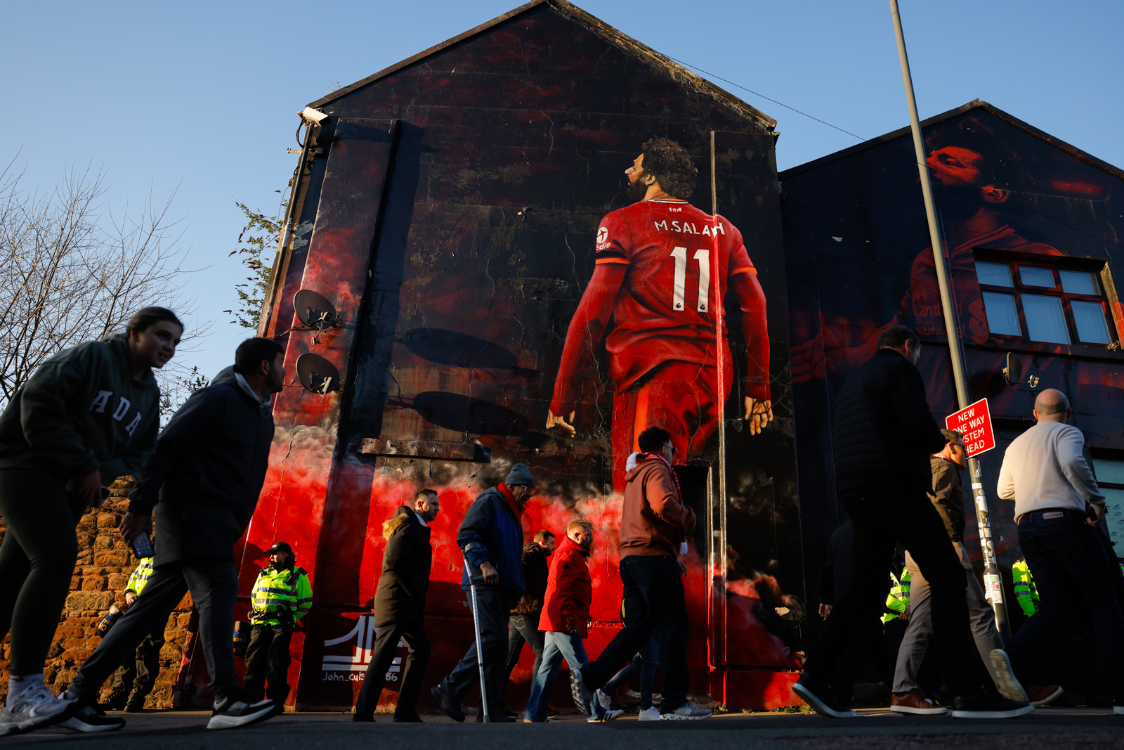 A photograph of Liverpool supporters walking past a mural of Mo Salah outside Anfield before a home game against local rivals Everton in April 2025