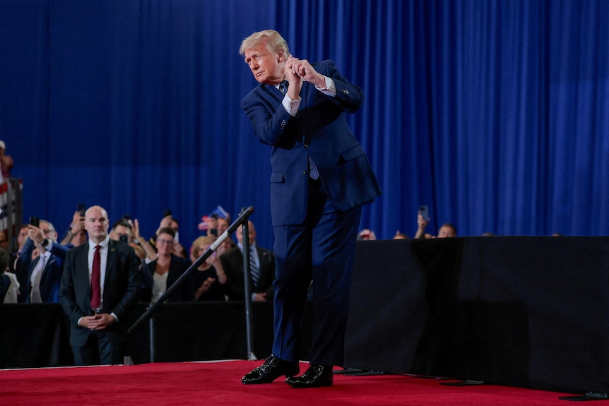 US President Donald Trump stands, tilting to the side, his two hands held up like he's swinging a golf club. 