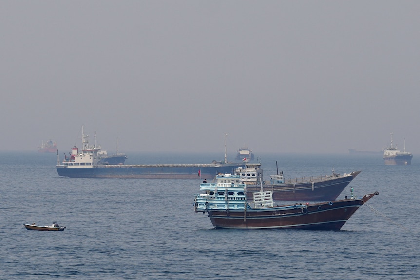 Three ships and a small dinghy on a body of water.