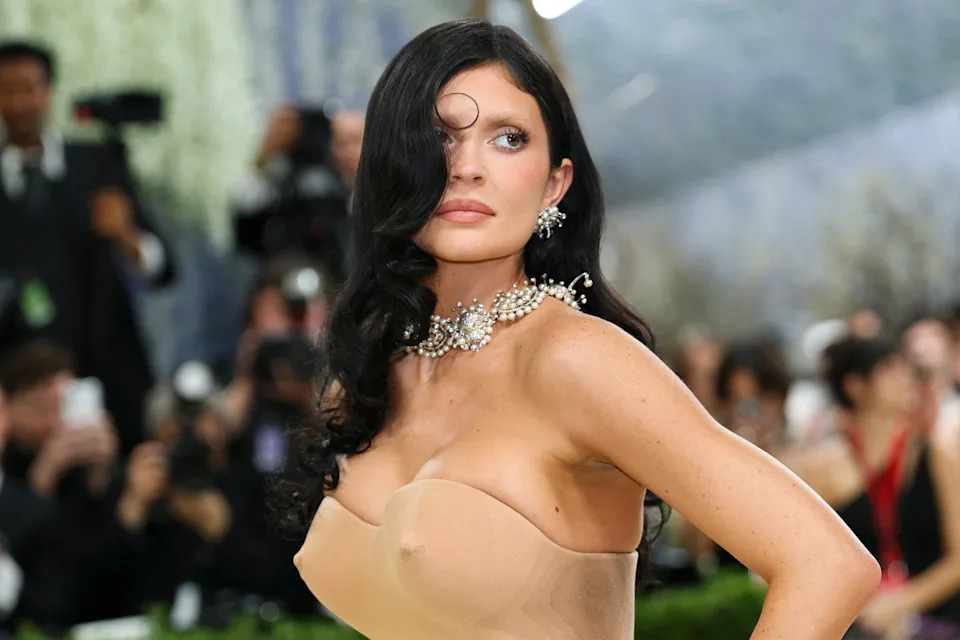 Kylie Jenner in an elegant strapless gown with ornate jewelry poses at a high-profile event, surrounded by photographers and attendees