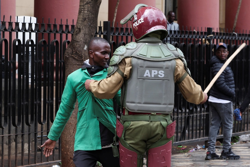 a police officer in riot gear pulls away a man in a green jacket on the street