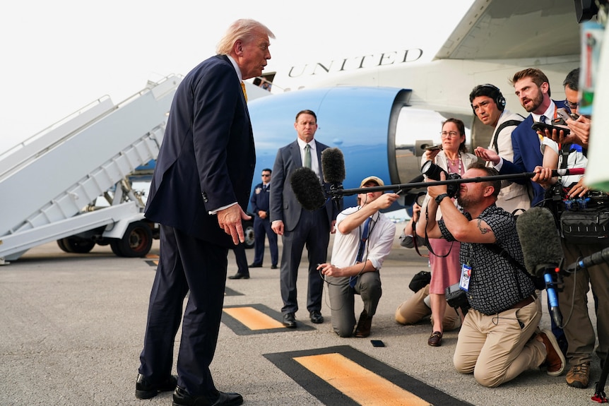 Donald Trump leans towards a group of reporters in front of the presidential plane Air Force One.