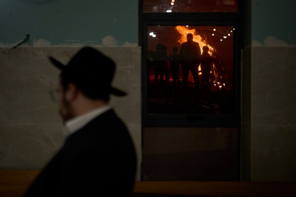 Ultra-Orthodox Jews are reflected in a window as they stand around a bonfire during Lag BaOmer, a holiday traditionally celebrated with bonfires, music, and gatherings, in Jerusalem, Monday, May 4, 2026. (AP Photo/Ohad Zwigenberg)