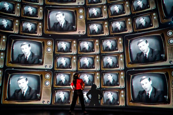 Head of creative enterprise, Maddie Hall, watches hundreds of television screens with broadcaster and naturalist David Attenborough's face, from when he was a young broadcaster, projected on a 360 degree screen inside the dome within the Market Hall ahead of a public release of an immersive film to mark his 100th birthday on May 8, at Real Ideas in Devonport, Plymouth, England, May 6, 2026. (Ben Birchall/PA via AP, File)