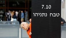 A protester against PM Benjamin Netanyahu in Tel Aviv, February, next to a sign reading '07.10, Netanyahu massacre.'
