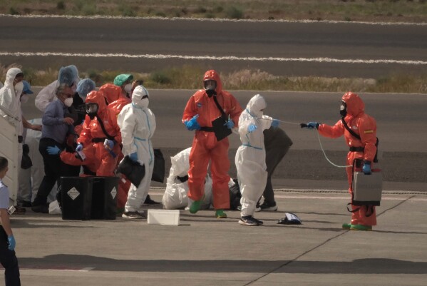 Passengers are sprayed with disinfectant by Spanish government officials before boarding a plane after disembarking from the hantavirus-stricken cruise ship MV Hondius at Tenerife airport in the Canary Islands, Spain, Sunday, May 10, 2026. (AP Photo/Arturo Rodriguez)