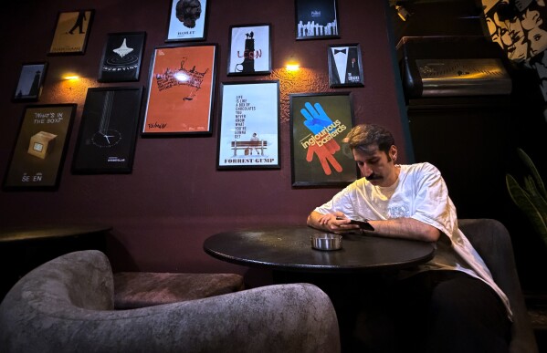 A man looks at his smart phone as he sits under posters of Hollywood movies at a cafe in Tehran, Iran, Friday, May 8, 2026. (AP Photo/Vahid Salemi)