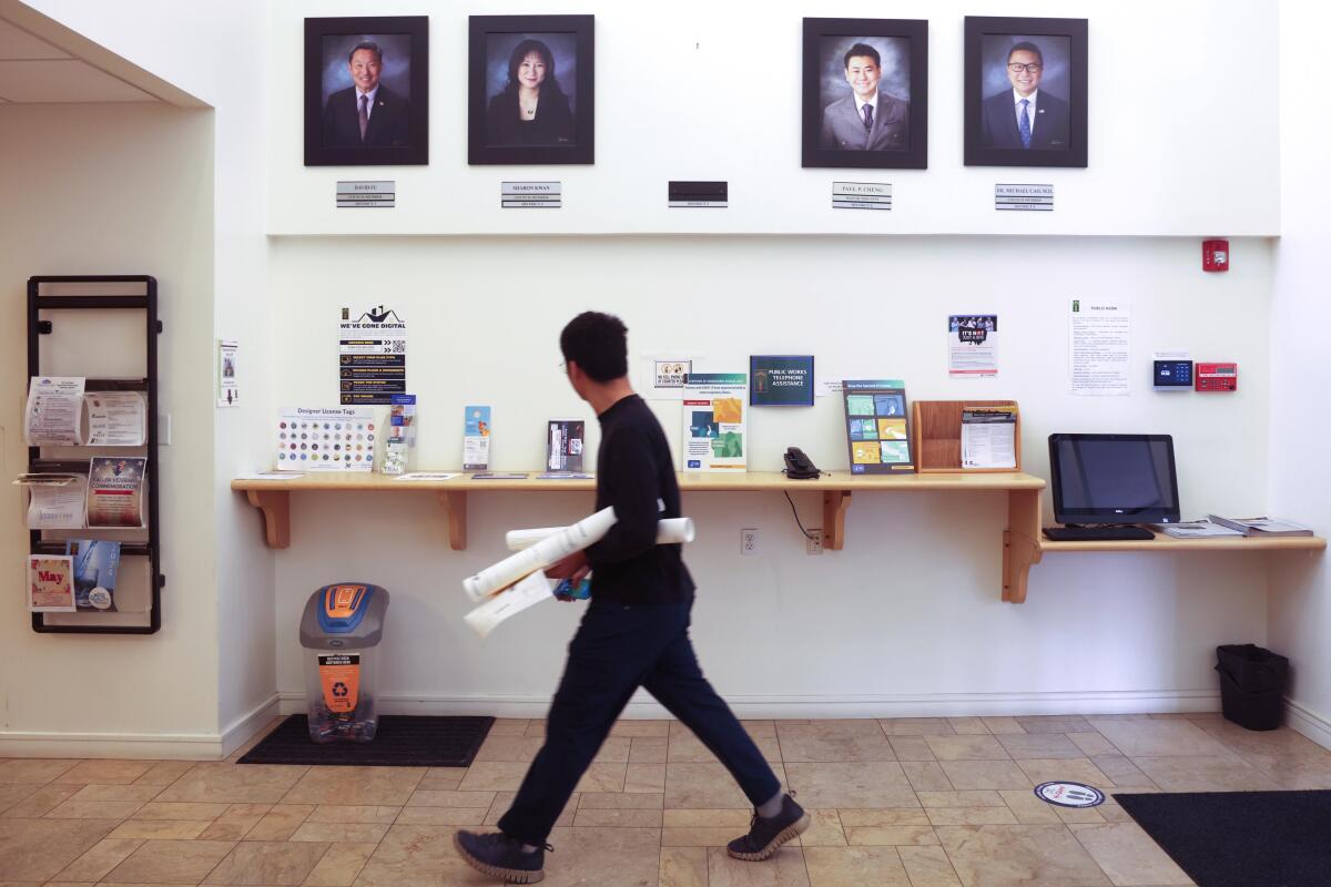 A man walks past an empty space where a photograph of former Arcadia Mayor Eileen Wang hung between other photos on a wall.