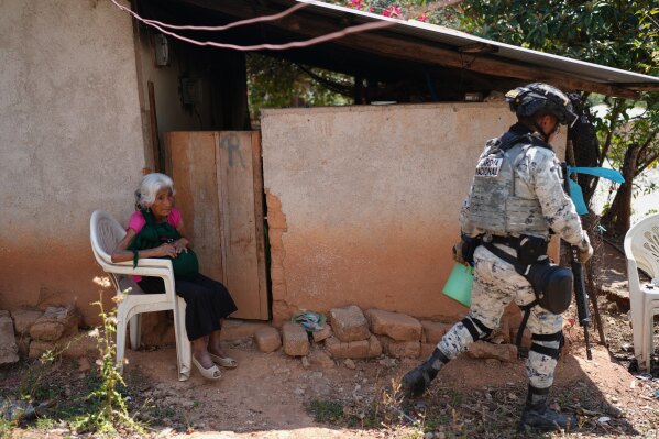 A National Guardsman walks past a resident sitting outside her home after armed attacks by local criminal groups forced more than dozens of residents to flee, in Tula, Mexico, Friday, May 15, 2026. (AP Photo/Marco Ugarte)
