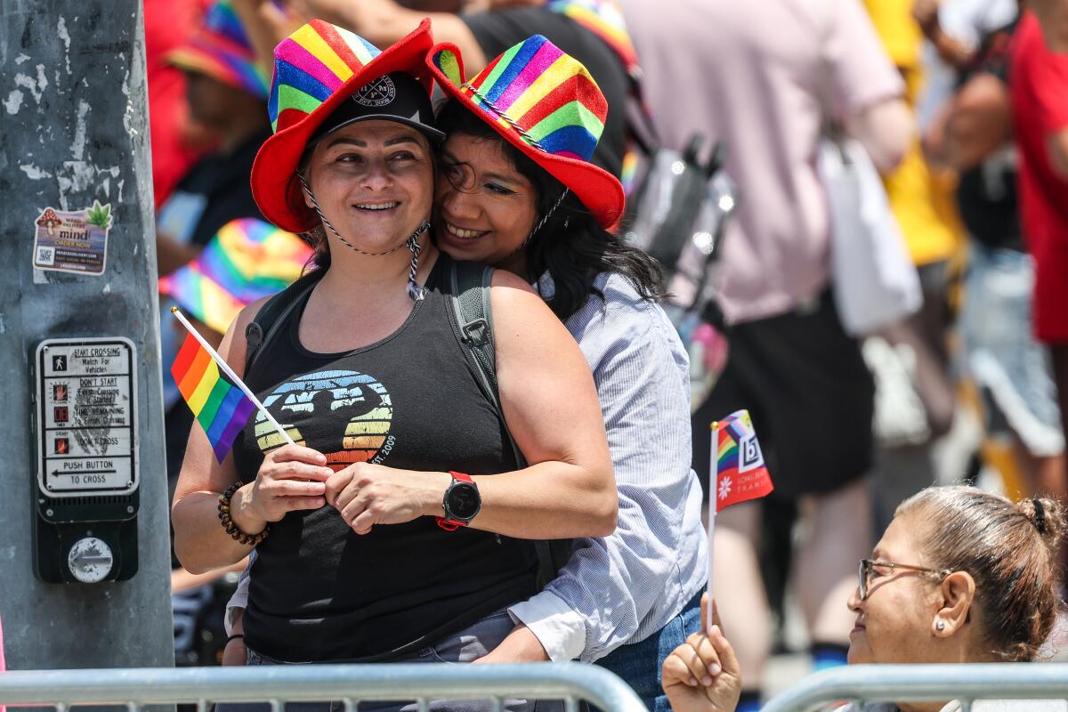 Two people in rainbow hats watch the Pride parade.