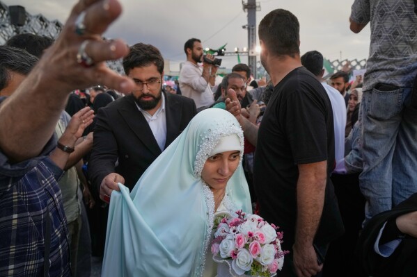 A bride and groom walk among attendants during a mass wedding ceremony for participants in the "Janfada" ("Sacrifice for Iran") pro-government campaign in Tehran, Iran, Monday, May 18, 2026. (AP Photo/Vahid Salemi)