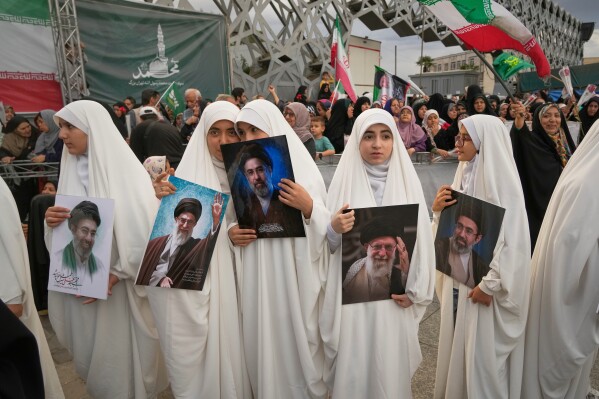 Girls hold portraits of Iran's Supreme Leader Ayatollah Mojtaba Khamenei and his late father, former Supreme Leader Ayatollah Ali Khamenei, as they watch a mass wedding ceremony for couples participating in the "Janfada," or "Sacrifice for Iran," pro-government campaign in Tehran, Iran, Monday, May 18, 2026. (AP Photo/Vahid Salemi)