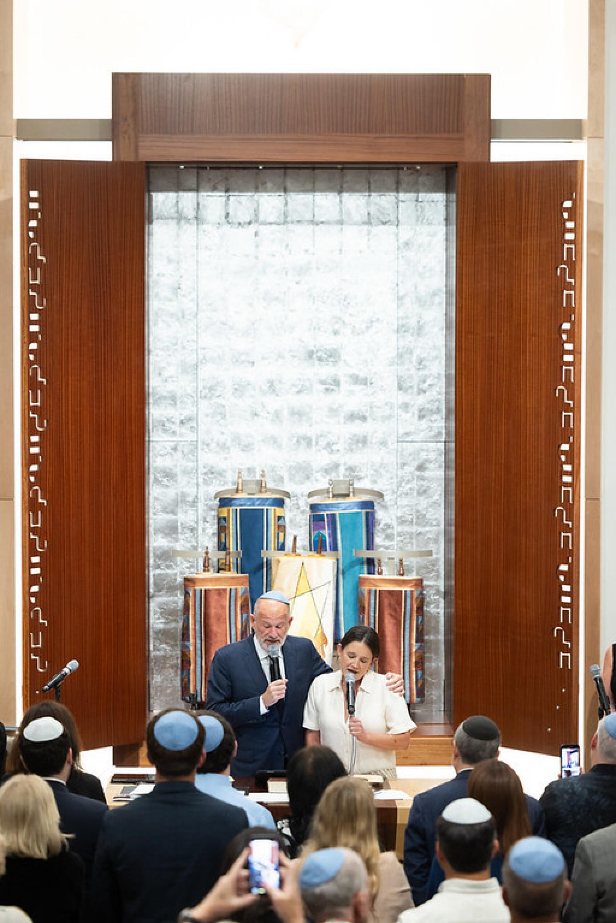 A father and daughter sing in front of a Torah ark.