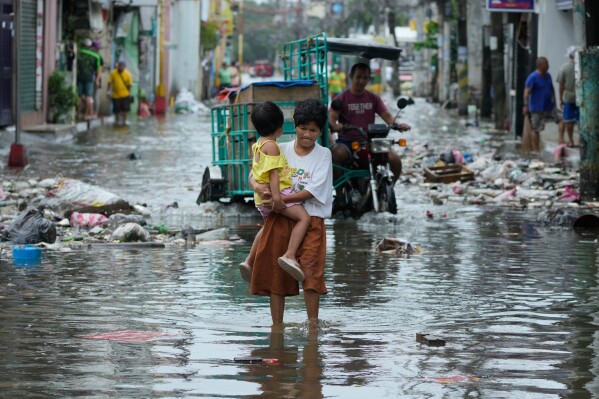 A woman and child crosses a flooded street due to Typhoon Fung-wong and high tide on Nov. 10, 2025, in Navotas, Philippines. (AP Photo/Aaron Favila, File)