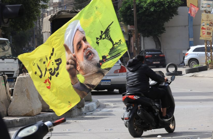 A person riding a scooter carries a flag with an image depicting Hezbollah leader Naim Qassem, as displaced people make their way to return to their homes after a 10-day ceasefire between Lebanon and Israel went into effect, at the southern suburbs of Beirut, Lebanon.