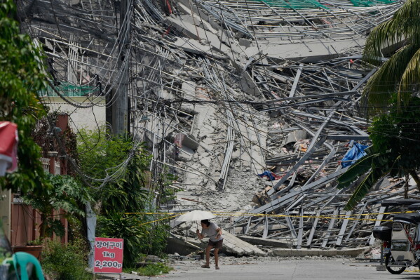 A woman walks beside a collapsed building where multiple people are believed to be trapped in Angeles city in Pampanga province, north of Manila Monday, May 25, 2026. (AP Photo/Aaron Favila)