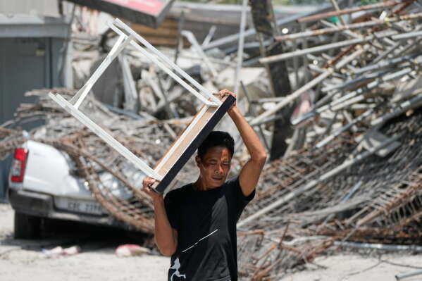 A man carries a table which he recovered from a damaged structure after a building collapsed where multiple people are believed to be trapped in Angeles city in Pampanga province, north of Manila Monday, May 25, 2026. (AP Photo/Aaron Favila)