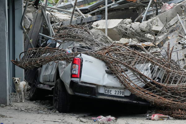 A dog stands beside a damaged pick-up truck at the ruins of a collapsed building where multiple people are believed to be trapped in Angeles city in Pampanga province, north of Manila, Philippines, Monday, May 25, 2026. (AP Photo/Aaron Favila)