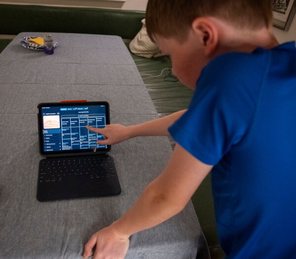 LuAnn Oliver's son demonstrates how he uses an iPad for his classes during a meeting where a group of school parents discussed ways to push back against screen time at the children's school, Saturday, May 9, 2026 in Arlington, Va. (AP Photo/Kevin Wolf)