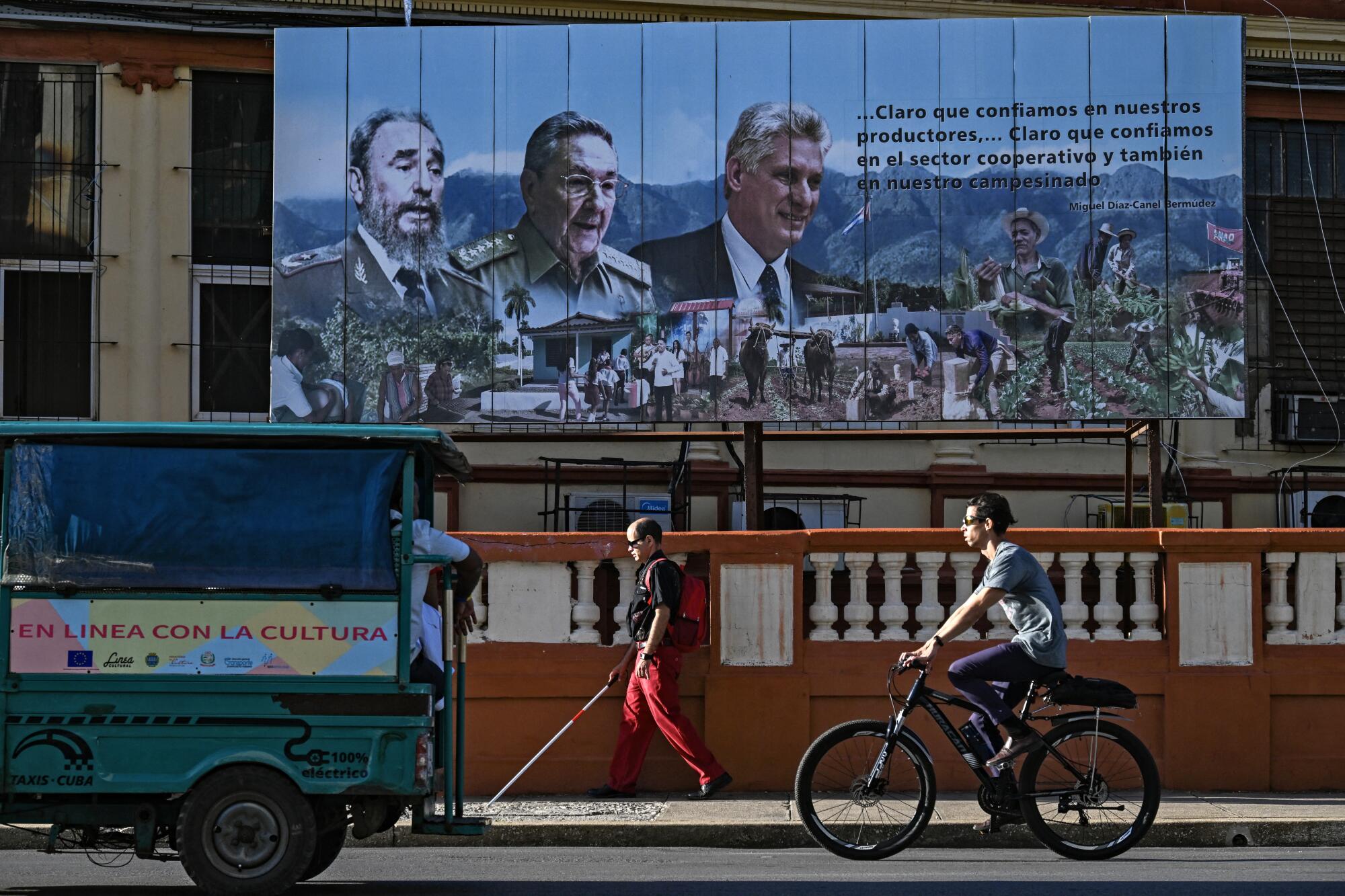 People pass a billboard depicting two men in military uniform and a third in dark suit and tie