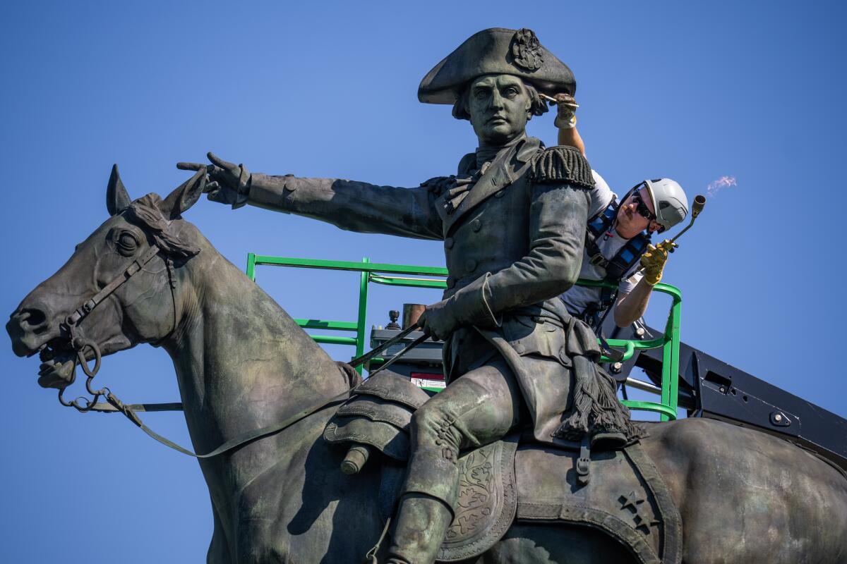 An employee does restoration work on a statue of a general on a horse