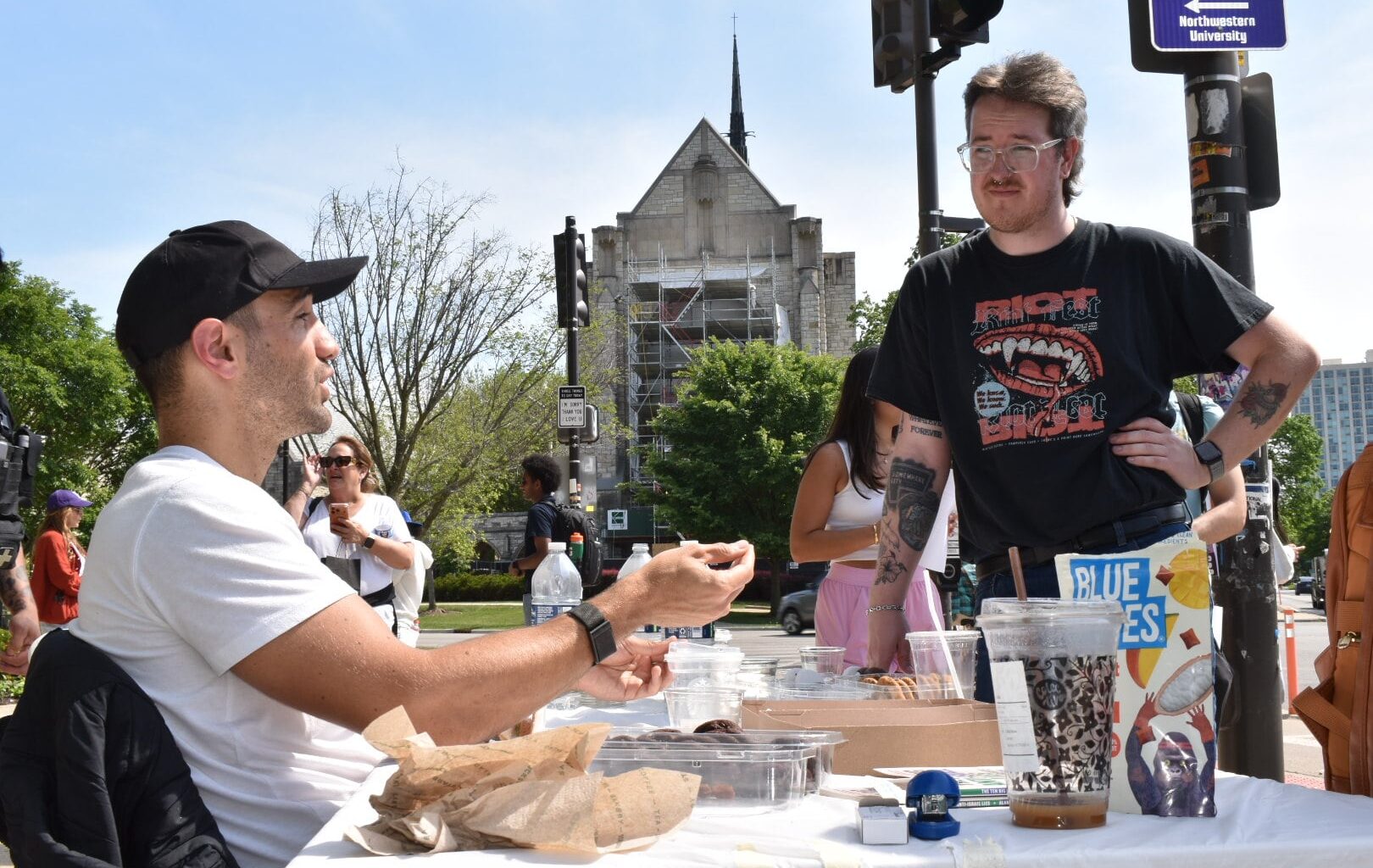A person sitting at a table speaks with a person standing on the other side of it.