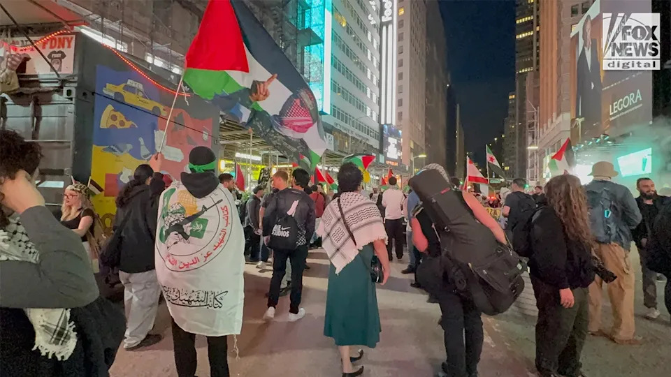 Demonstrators carrying imagery of Abu Obaida and Palestinian flags in Times Square New York City