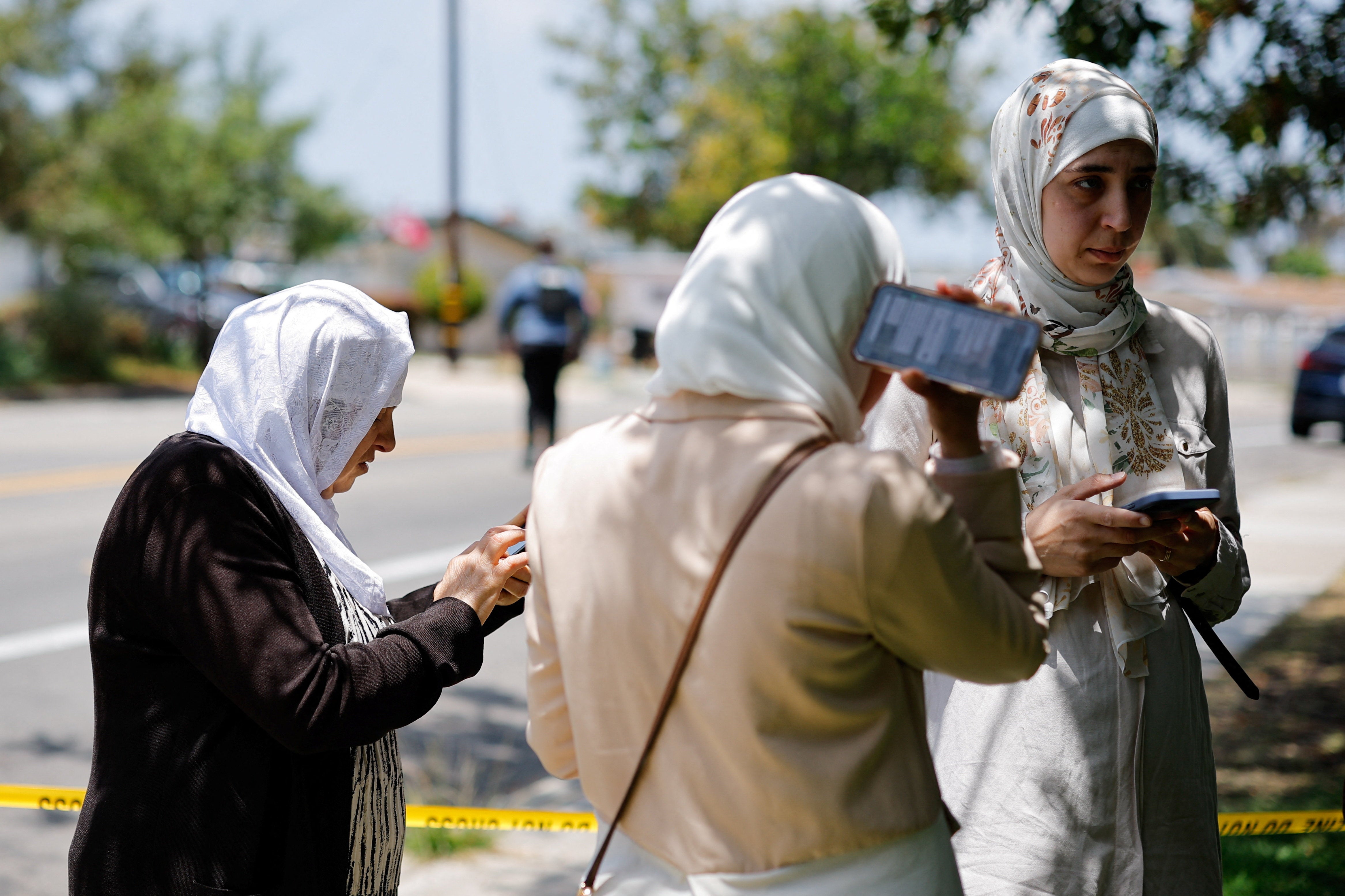 Members of the Muslim community use their phones at the scene of a reported active shooter situation at the Islamic Center