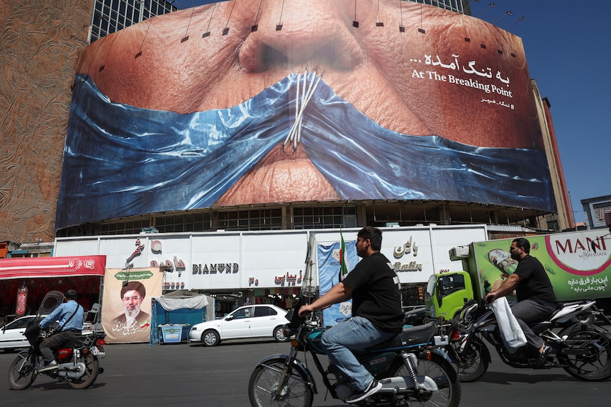 People ride past an anti-US billboard depicting US President Donald Trump
