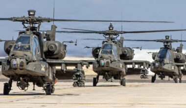 Three military helicopters sit near each other on a cement airfield.