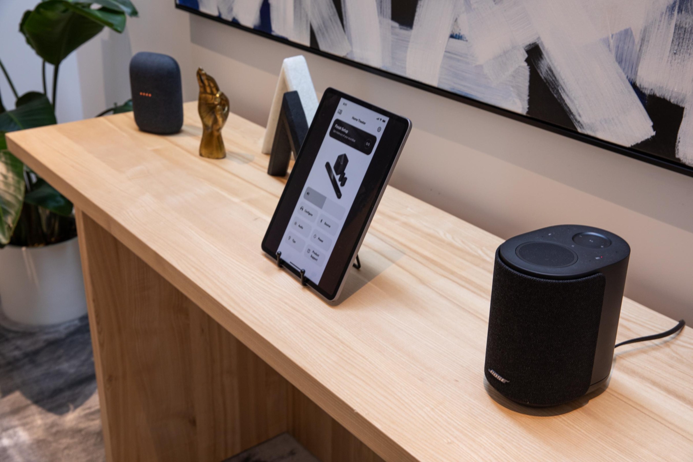 The Bose Ultra Speaker on a wooden table next to a tablet and a Google Nest speaker.