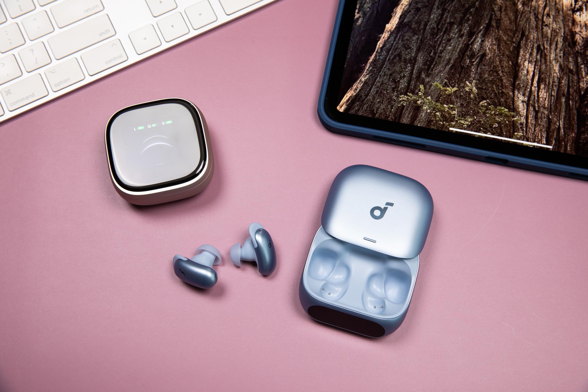 The Soundcore Liberty 5 Pro and 5 Pro Max on a mauve background next to an iPad and Apple keyboard.