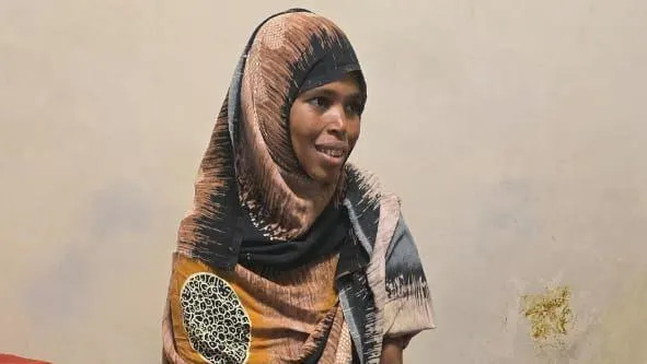 Close-up of Bedriya smiling. She is wearing a patterned printed green and yellow head covering.