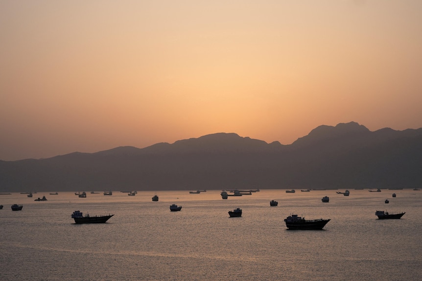 Sun setting behind a mountain as ships and boats sit in the ocean.