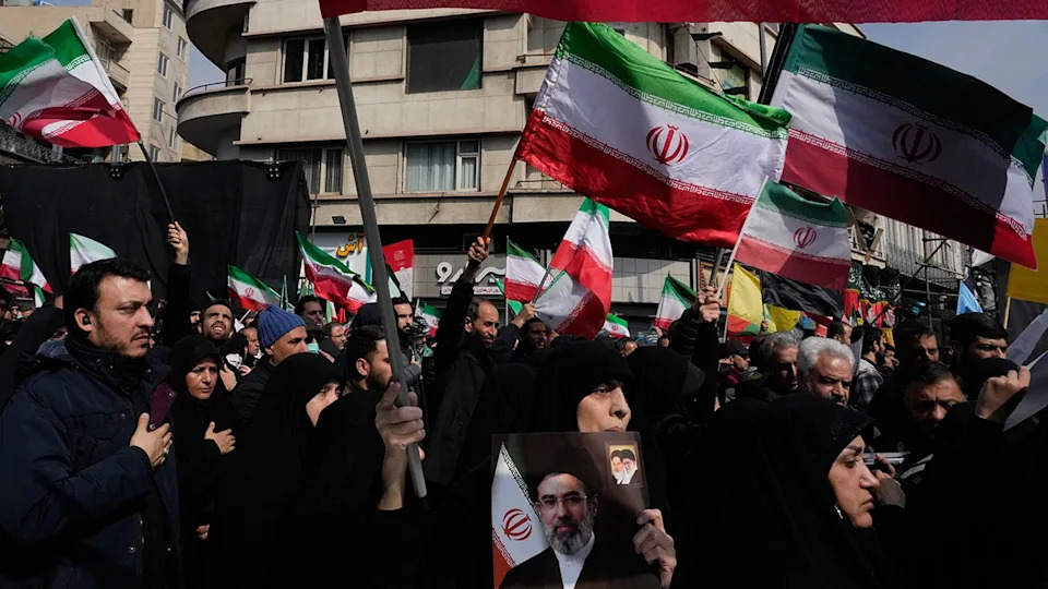 Mourners waving Iranian flags and holding a poster of Ayatollah Mojtaba Khamenei in Tehran