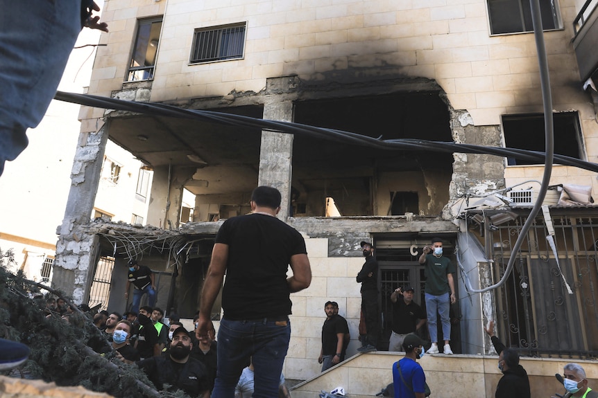 A crowd of men inspect a massive hole in the side of a building.