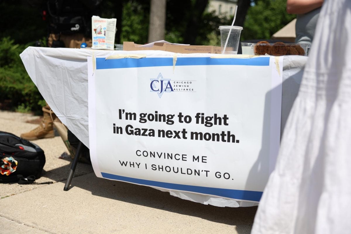 A banner taped to the front of a table reads “I’m going to fight in Gaza next month. CONVINCE ME WHY I SHOULDN’T GO.”