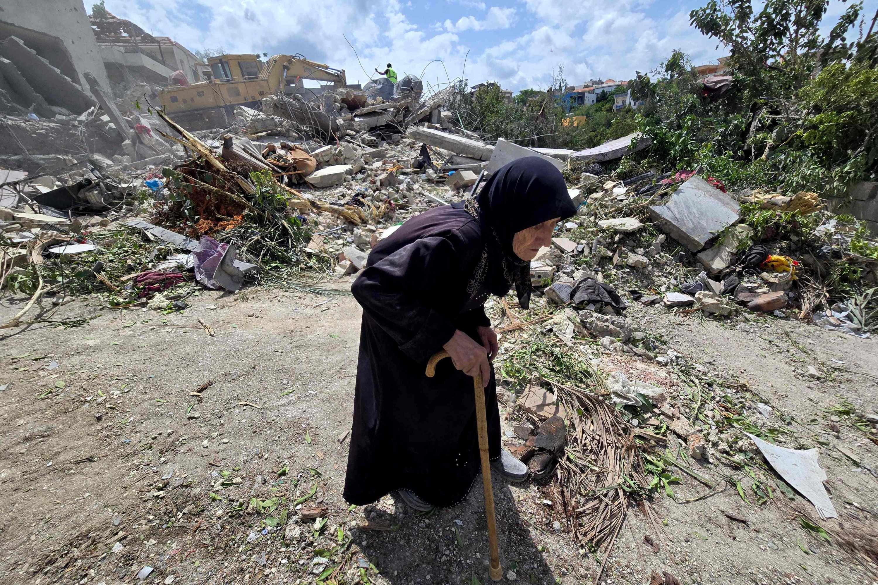 An elderly woman walks past Lebanese civil defense workers searching through the rubble in the village of Deir Qanun al-Nahr, southern Lebanon, May 20, 2026. (AFP Photo)