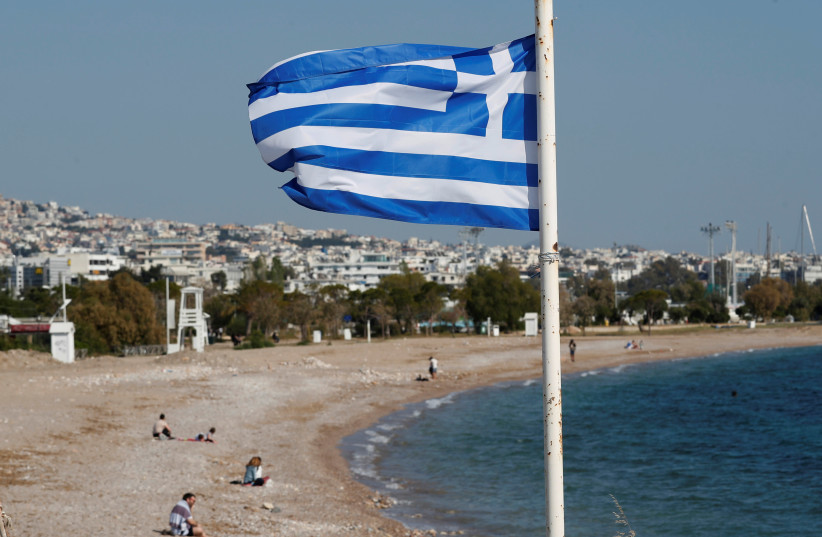 A Greek national flag flutters as people visit a beach in April 28, 2020.