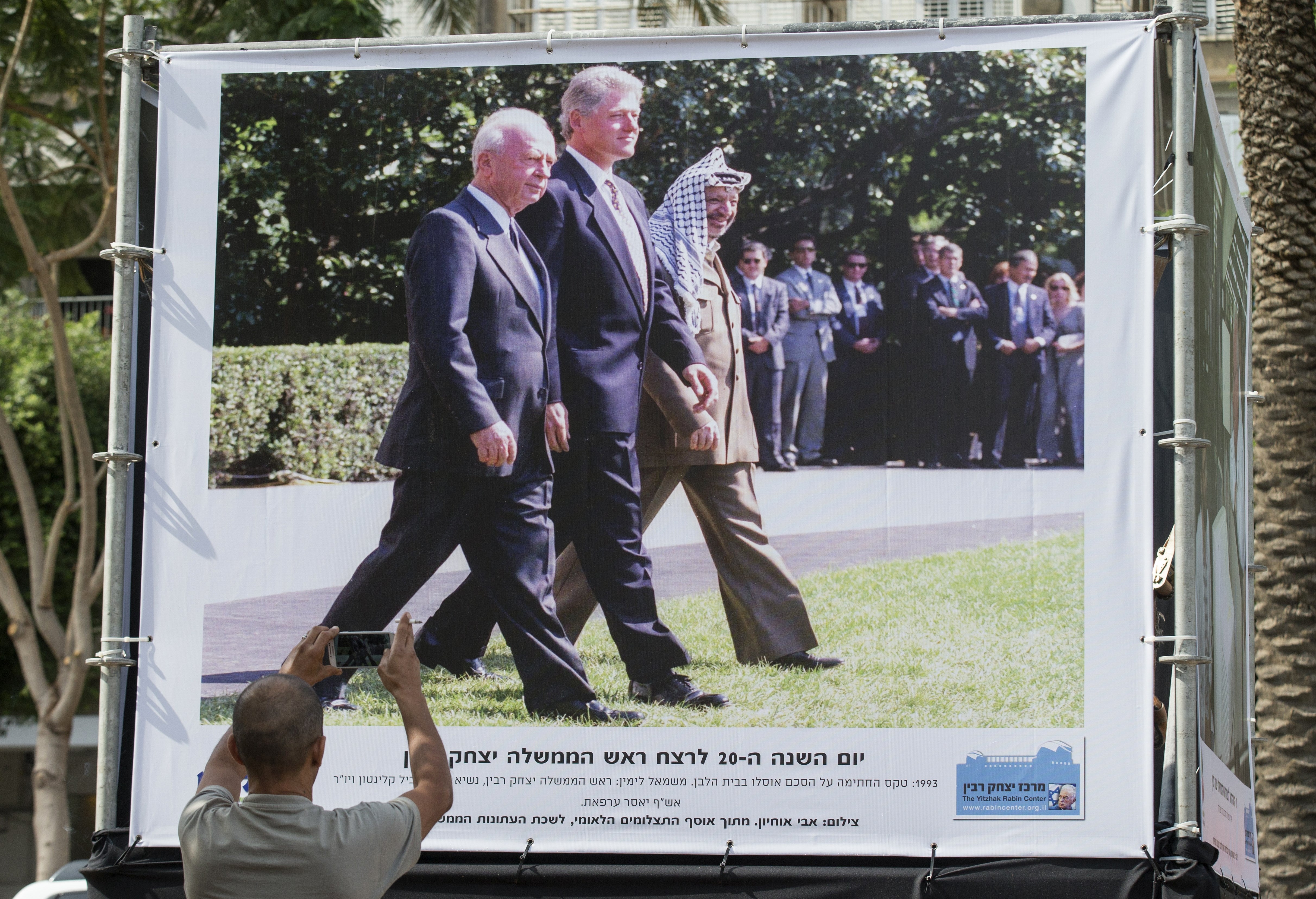 A man takes a picture of a photograph taken by Israeli Government Press Office Avi Ohayon showing late Israeli prime minister Yitzhak Rabin (L) walking alongside former US president Bill Clinton and later Palestinian leader Yasser Arafat, displayed at an exhibition marking the 20th anniversary of Rabin's assassination, on October 26, 1995