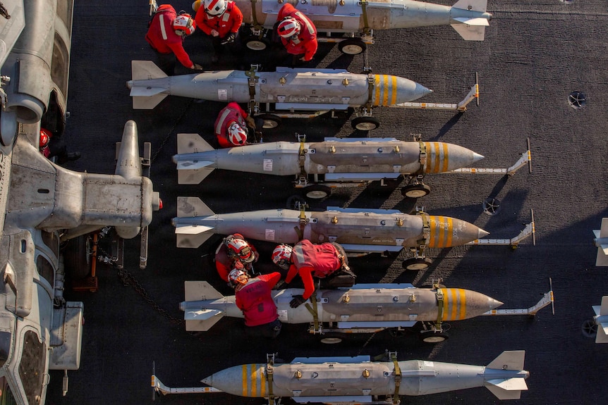 An overhead view of US Navy sailors performing work on missiles aboard the deck of a ship