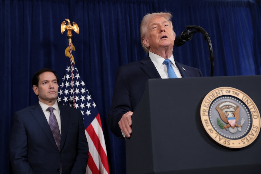 Trump grasps the sides of a podium as he speaks into a microphone in front of Marco Rubio.