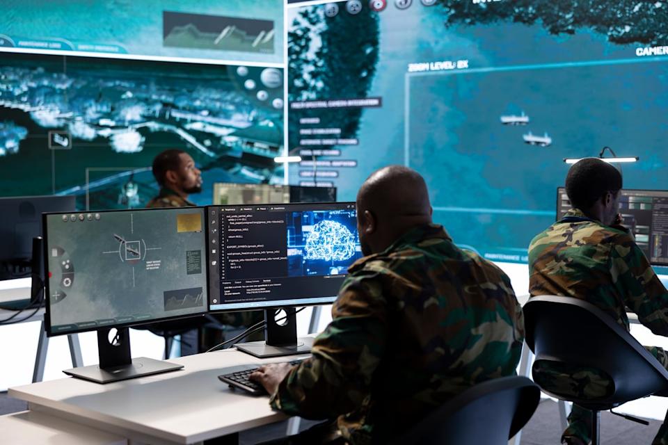 Military soldiers at computer screens monitor satellite imaging.
