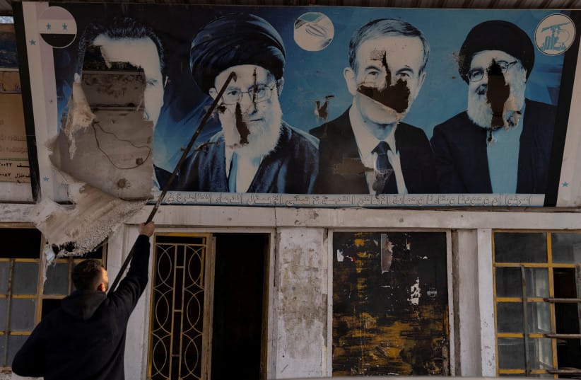 A worker tears down the pictures of Syria's Bashar al-Assad, former Syrian President Hafez al-Assad, Lebanon's late Hezbollah leader Sayyed Hassan Nasrallah and Iran's Supreme Leader Ayatollah Ali Khamenei at a gas station in Nubl, in rural Aleppo, Syria, December 11, 2024.