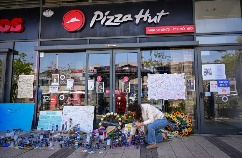 People gather outside a Pizza Hut branch in Petah Tikva, lighting candles and placing flowers in memory of employee Yemanu Binyamin Zalka, who was stabbed and later died of his wounds on the eve of Independence Day, April 27, 2026
