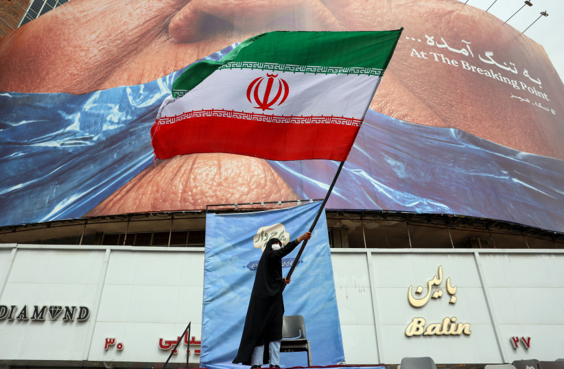 A woman waves an Iranian flag in front of an anti-US billboard referring to US President Donald Trump and the Strait of Hormuz at Valiasr Square in Tehran on May 5, 2026.
