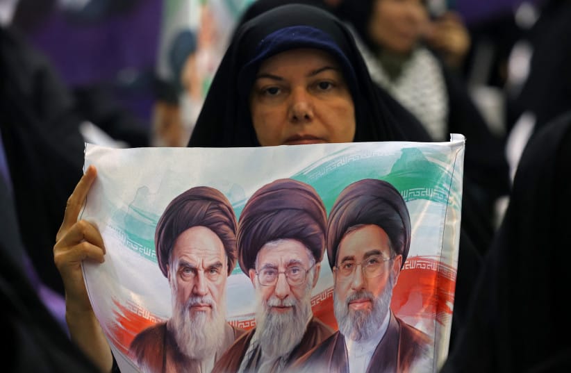 An Iranian woman holds a banner of the three Iranian supreme leaders imposed over the Islamic Republic's flag at an anti-Israel and anti-US event in Tehran, May 24, 2026; illustrative.